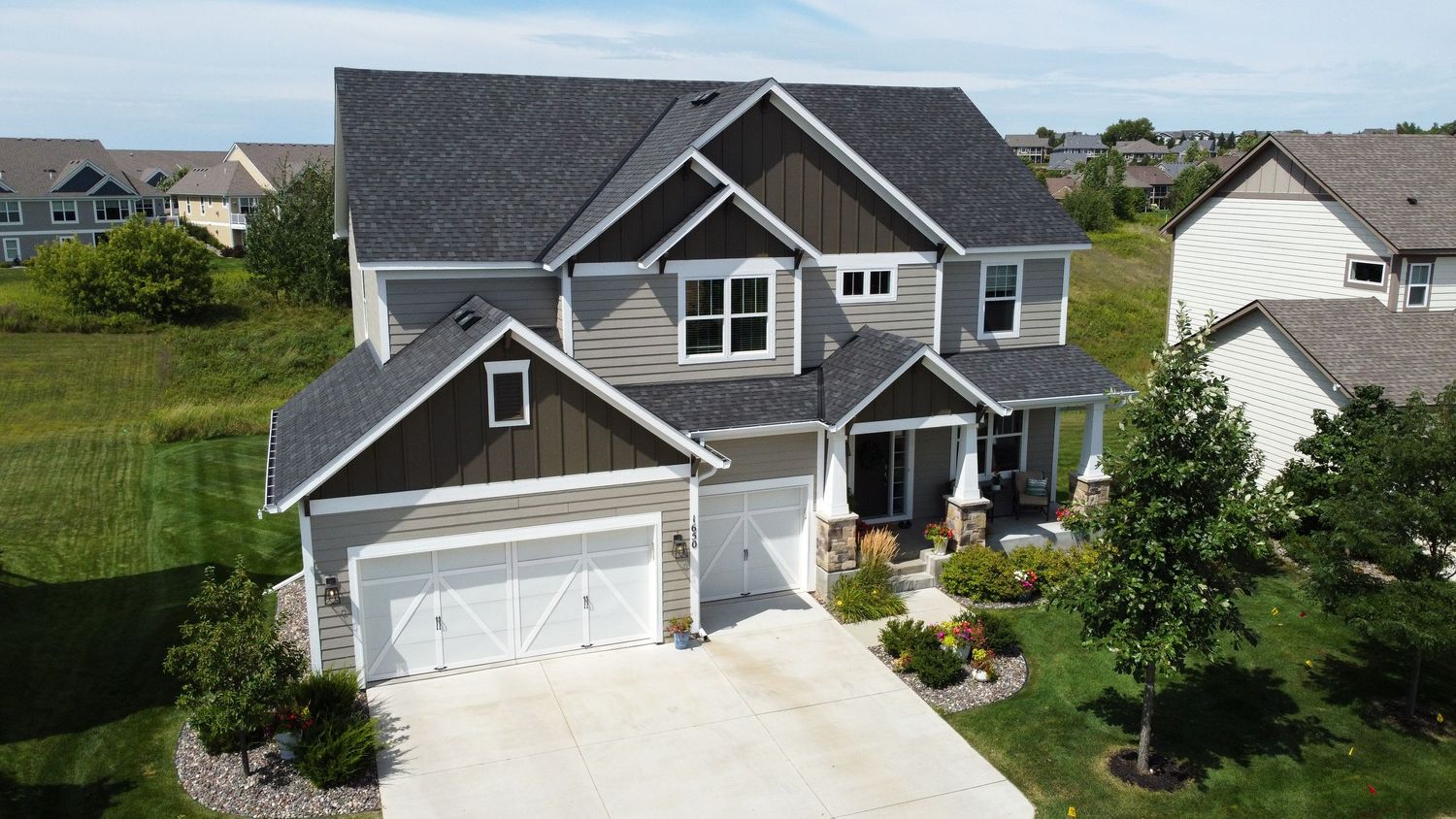 Gray and white craftsman style house with three car garage and landscaped front yard.