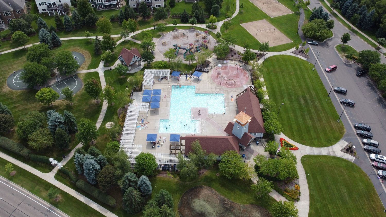 Aerial view of a community pool complex with water features and landscaping surrounded by green space.