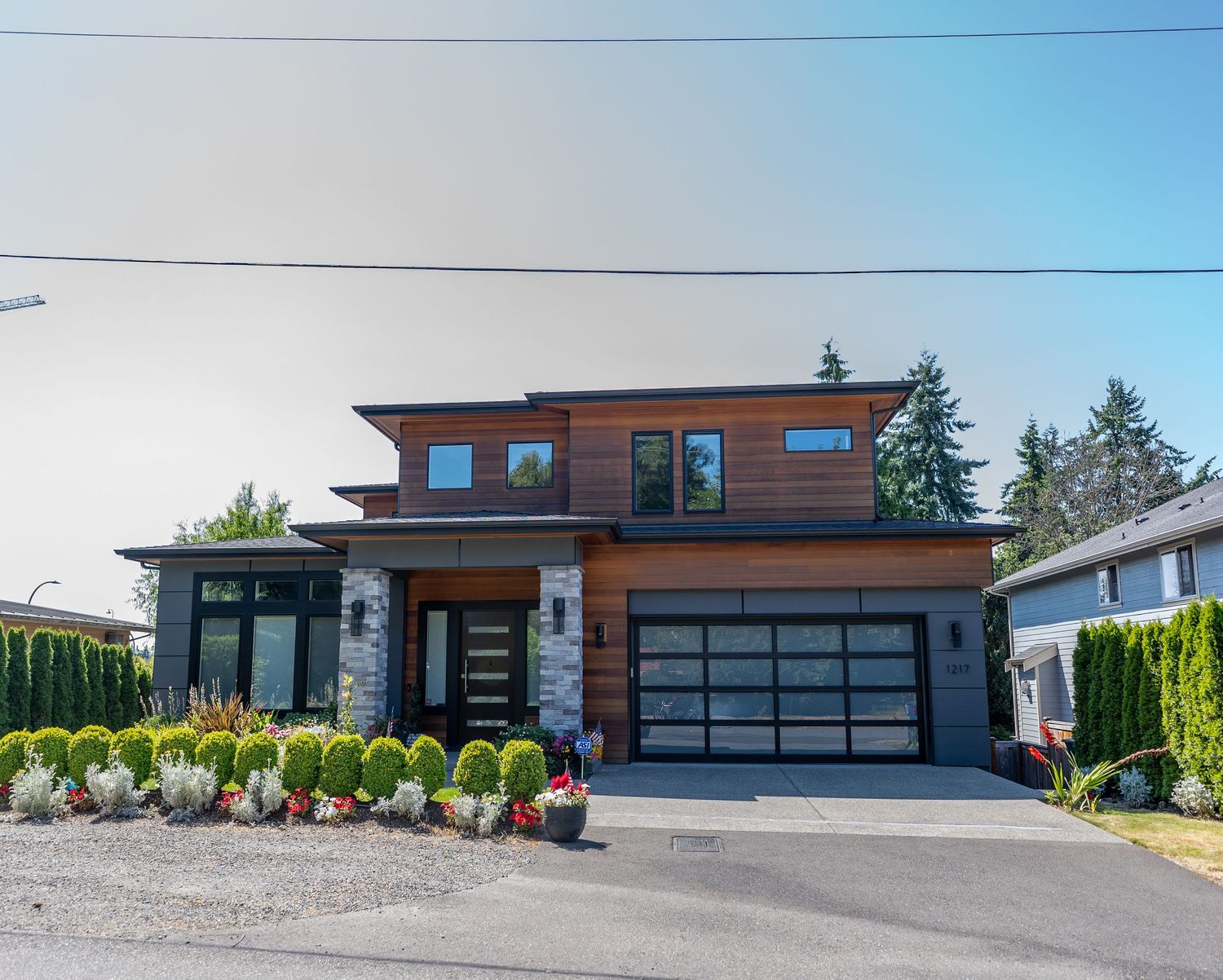 Modern two-story home with cedar siding, glass garage door, and landscaped front yard featuring ornamental grasses.