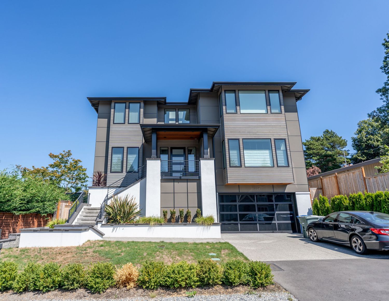 Contemporary three-level luxury home with white and wood accents, glass railings, and double garage.