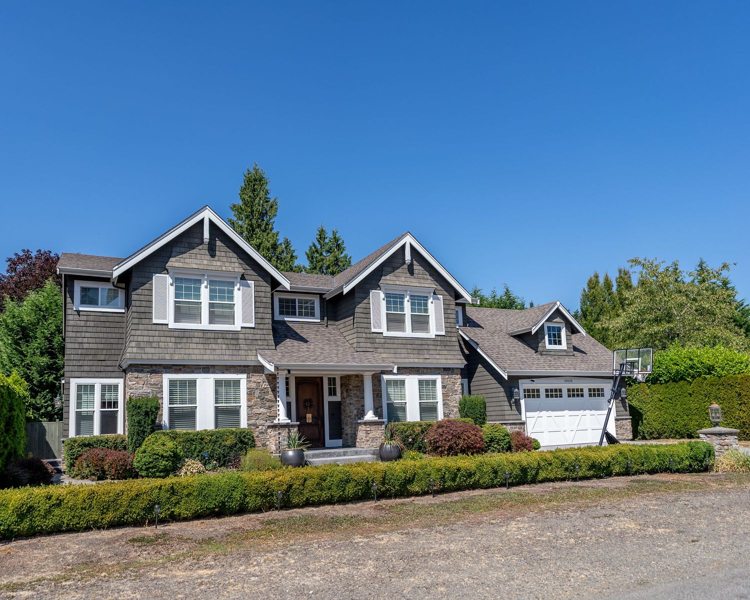 Traditional craftsman style home with stone accents, twin gables, and attached garage surrounded by lush landscaping.