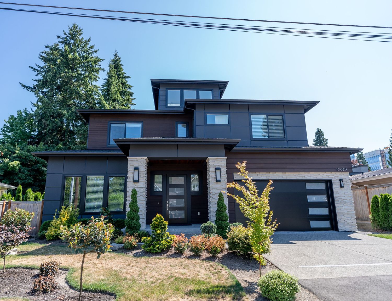 Contemporary dark-colored house with glass garage doors, angular roofline, and modern landscaping design.
