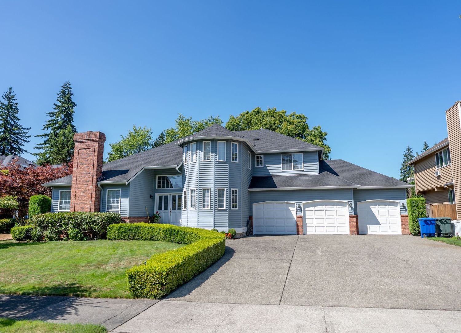 Luxury curved facade home with grey exterior, triple car garage, and manicured hedges.