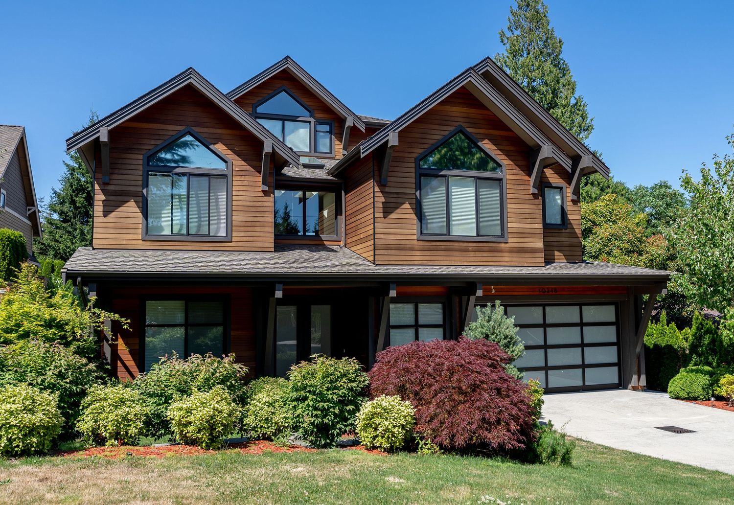 Modern craftsman style home with brown exterior, large windows, and landscaped front yard on sunny day.