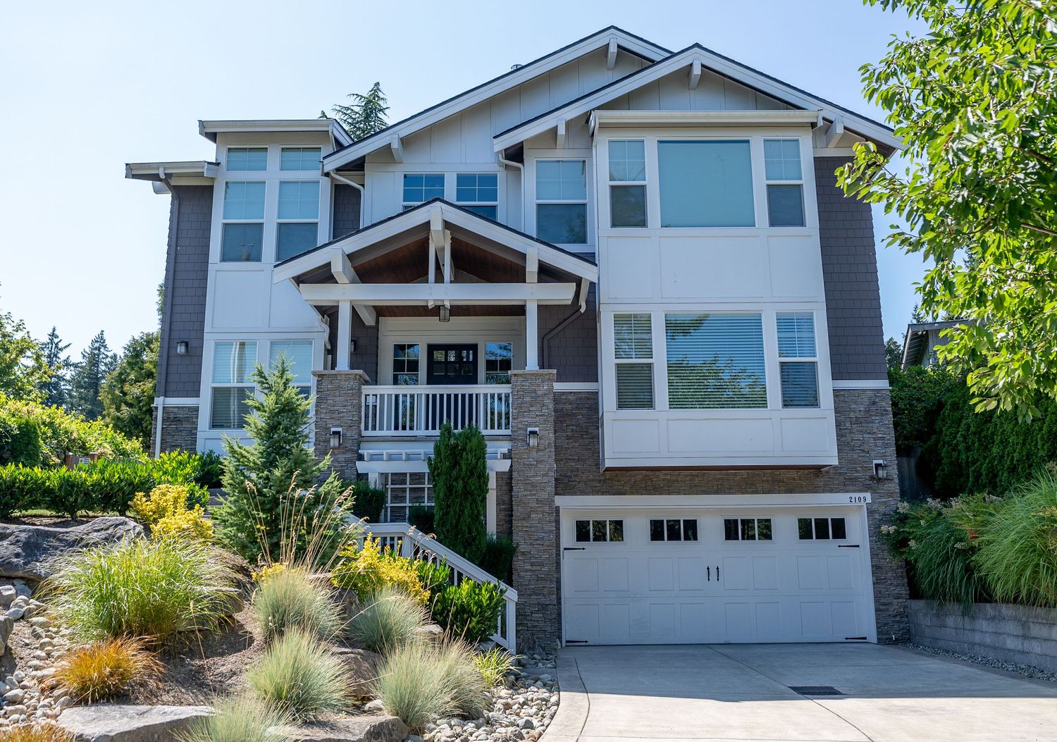 Gray modern house with stone accents, covered porch, and three-car garage built on hillside.