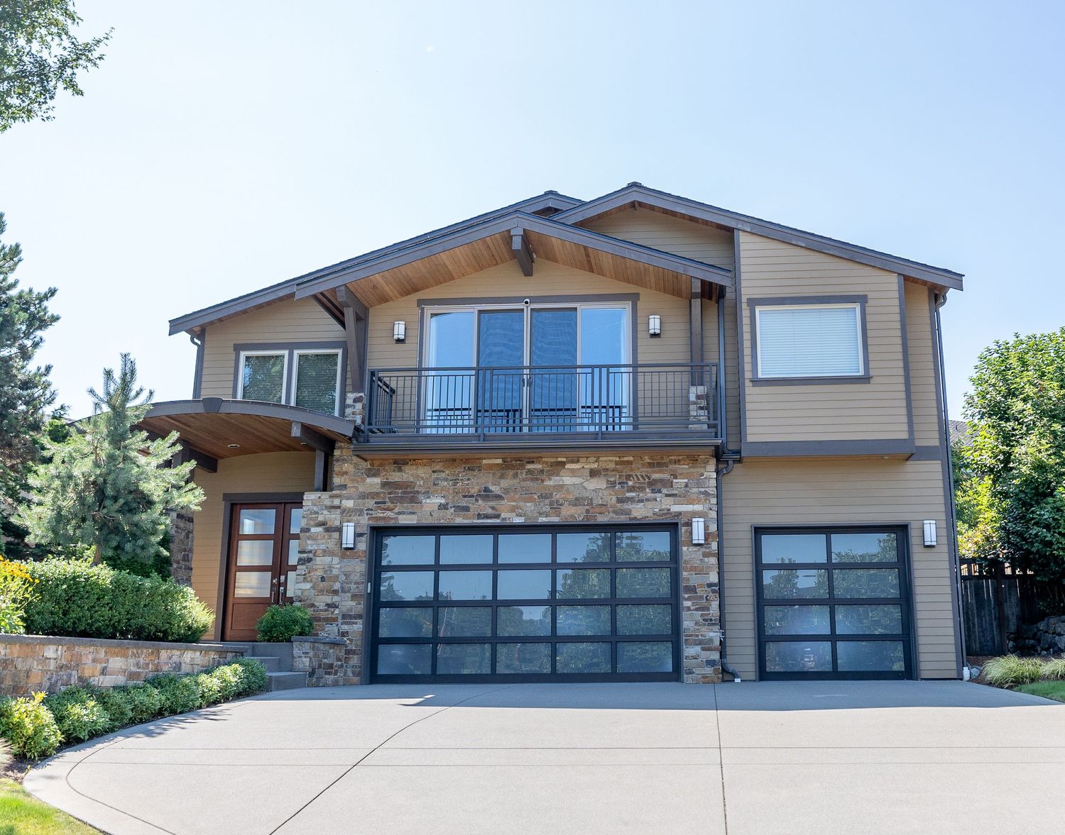 Contemporary two-story house with stone accent wall and glass garage doors on sloped driveway.
