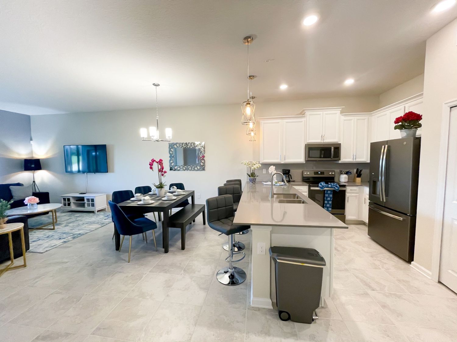 Modern open concept living space with kitchen island, pendant lights and gray furniture.