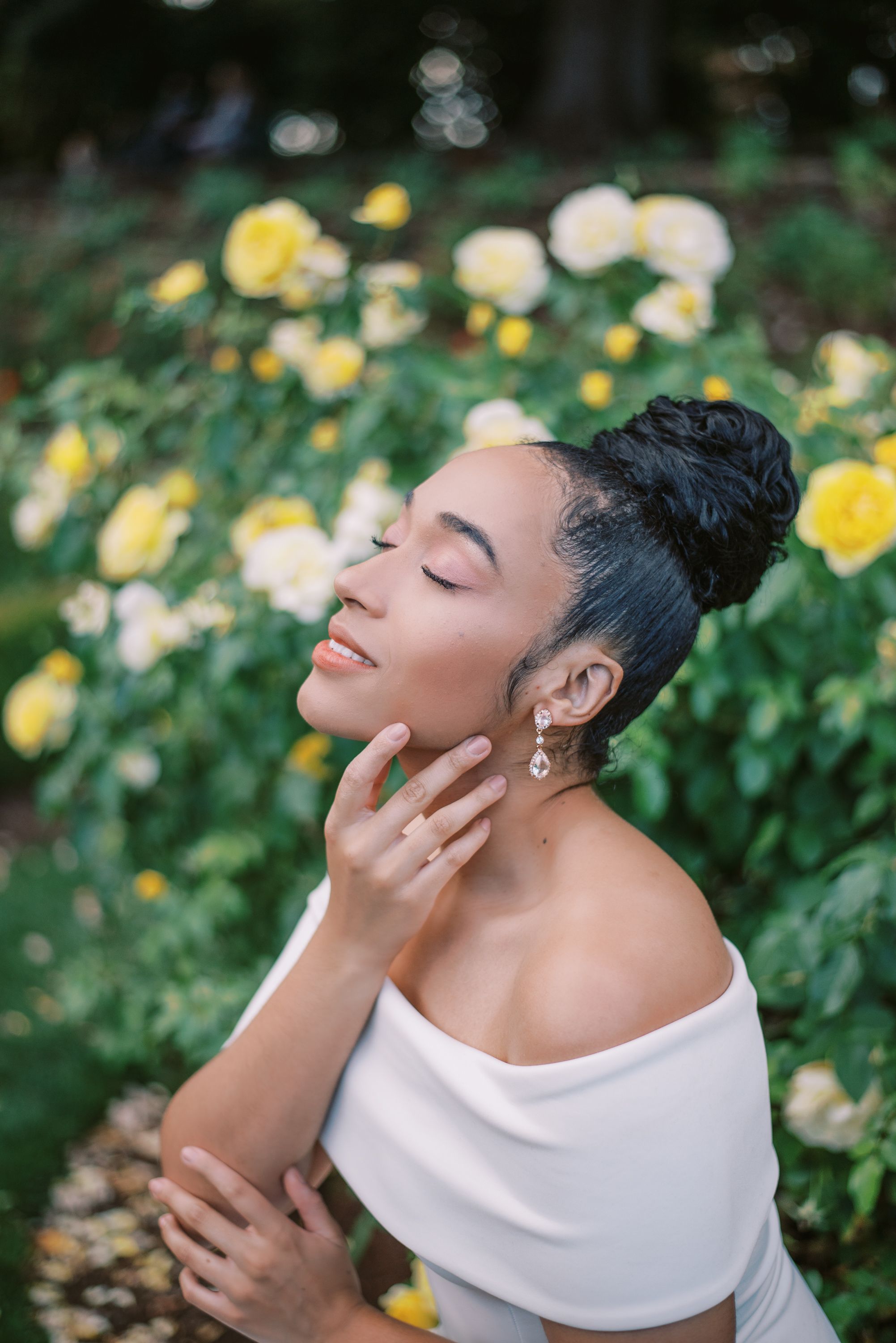 Serene garden portrait with yellow roses and a classic white off-shoulder dress.