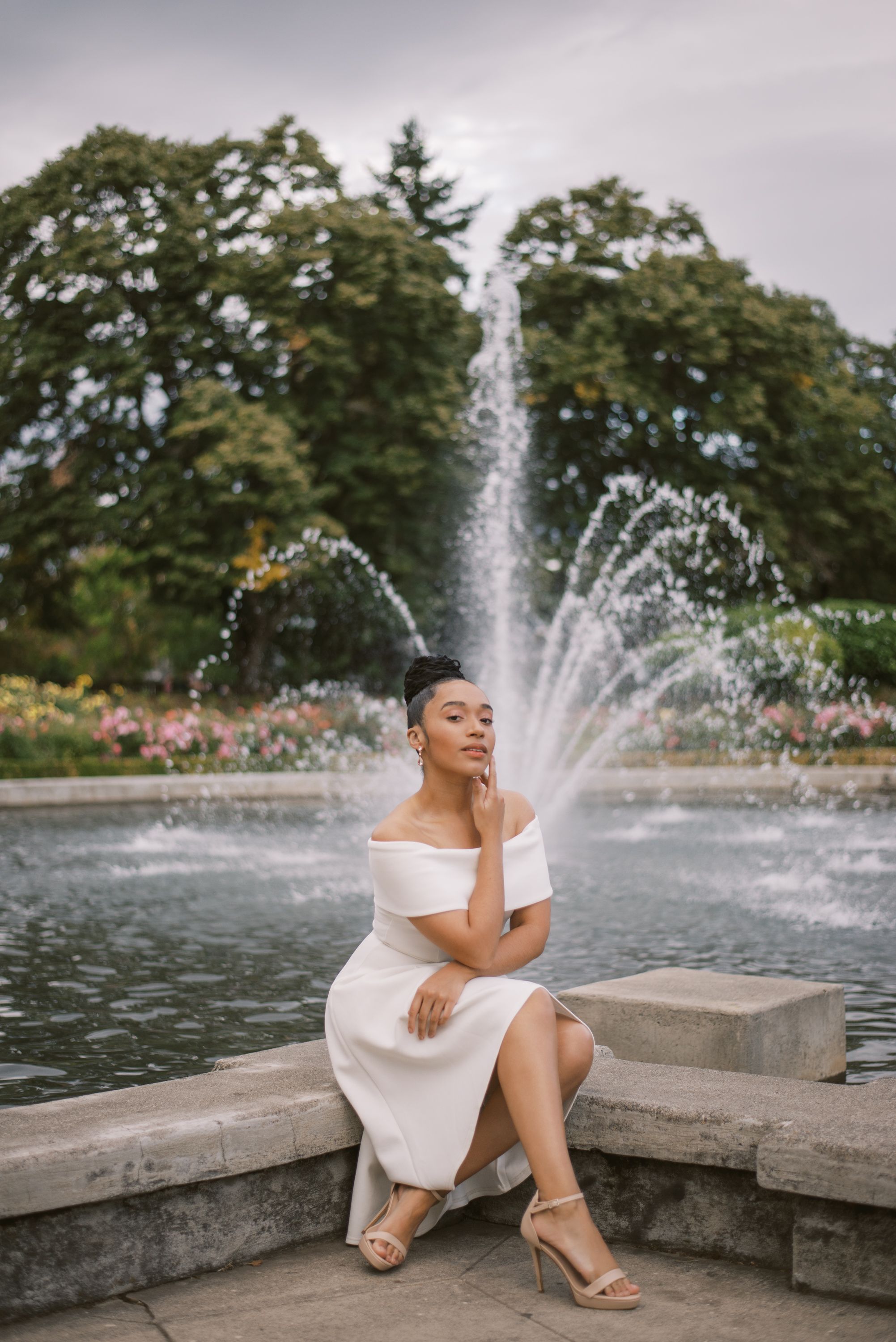 White dress creates elegant scene by fountain in garden with water sprays and stone ledge.