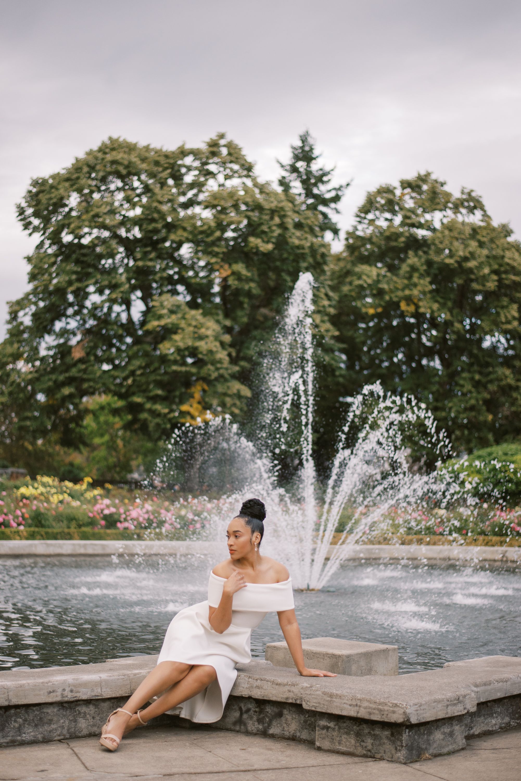 Graceful pose on stone ledge with cascading fountain and garden backdrop.