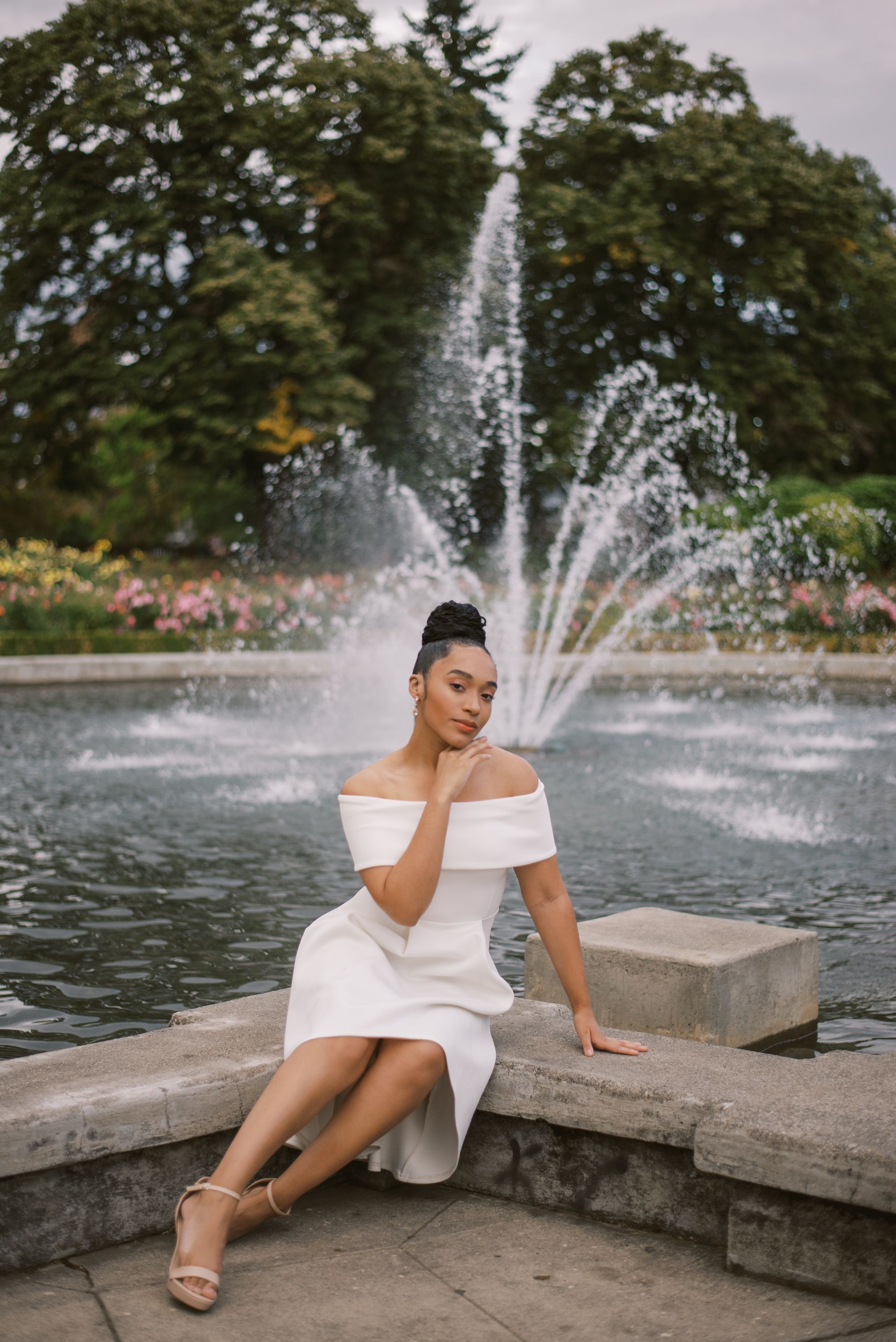 Off-shoulder white dress portrait against fountain with water features.