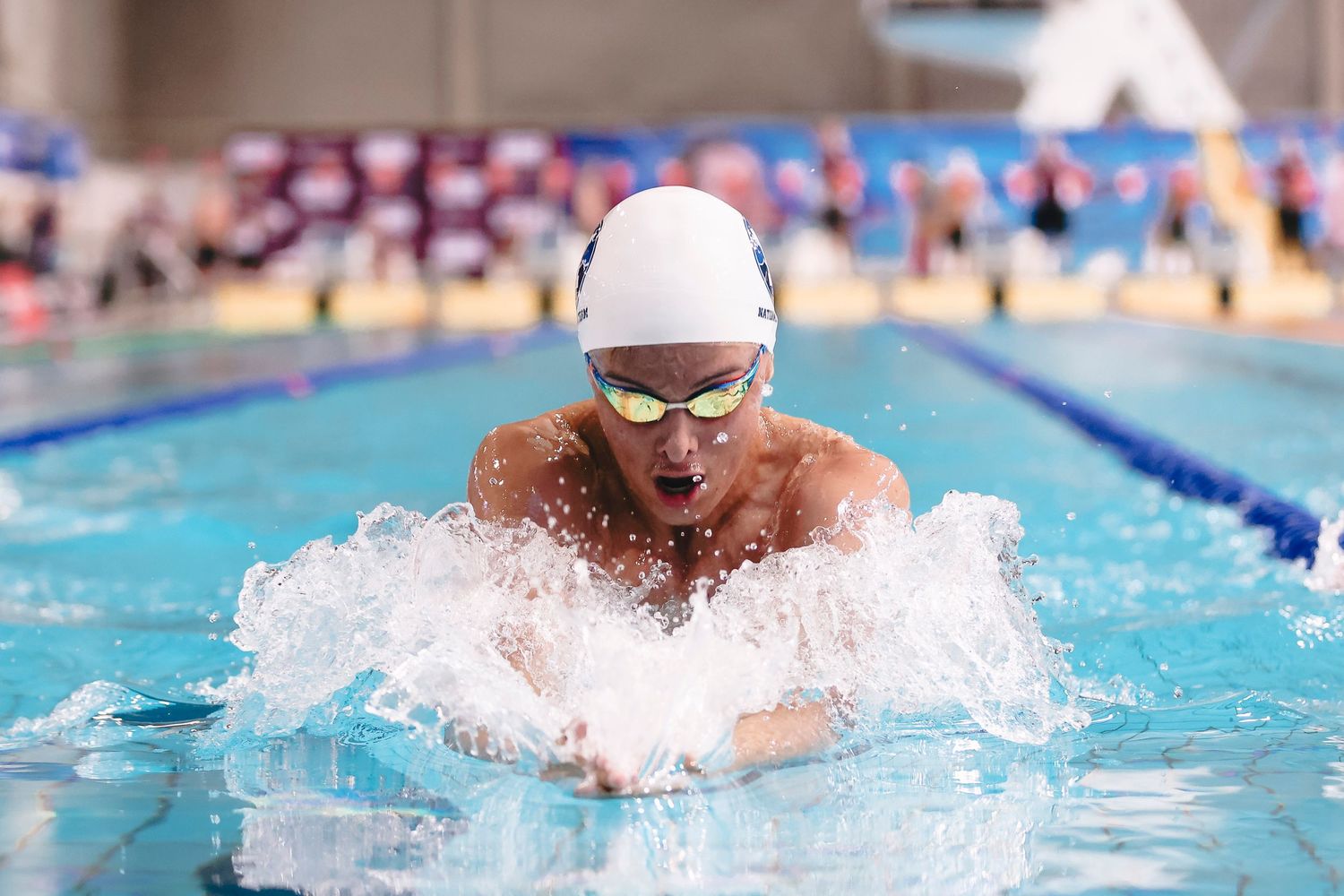 Swimmer performing breaststroke with water splashing in competitive pool.