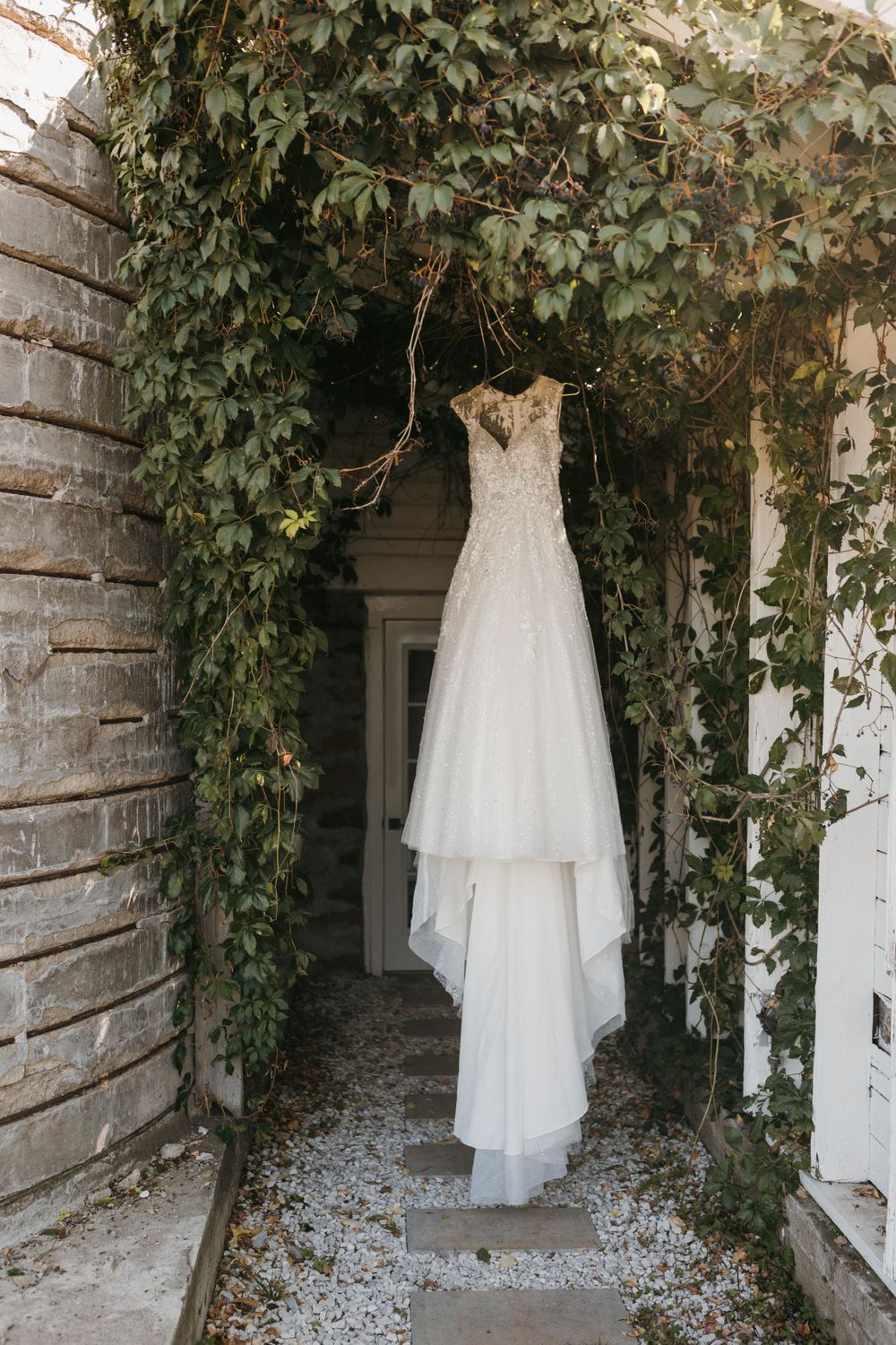 White lace wedding dress hanging under an ivy-covered archway at a charming outdoor venue.