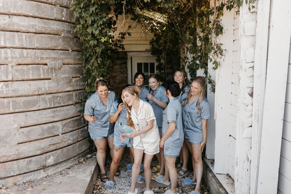 Bride and bridesmaids in blue rompers walking through charming ivy-covered outdoor passageway.