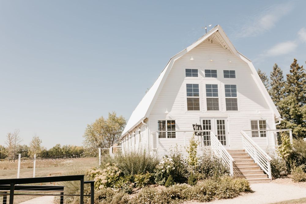 Stunning white barn wedding venue with large windows and manicured landscaping under a blue sky.