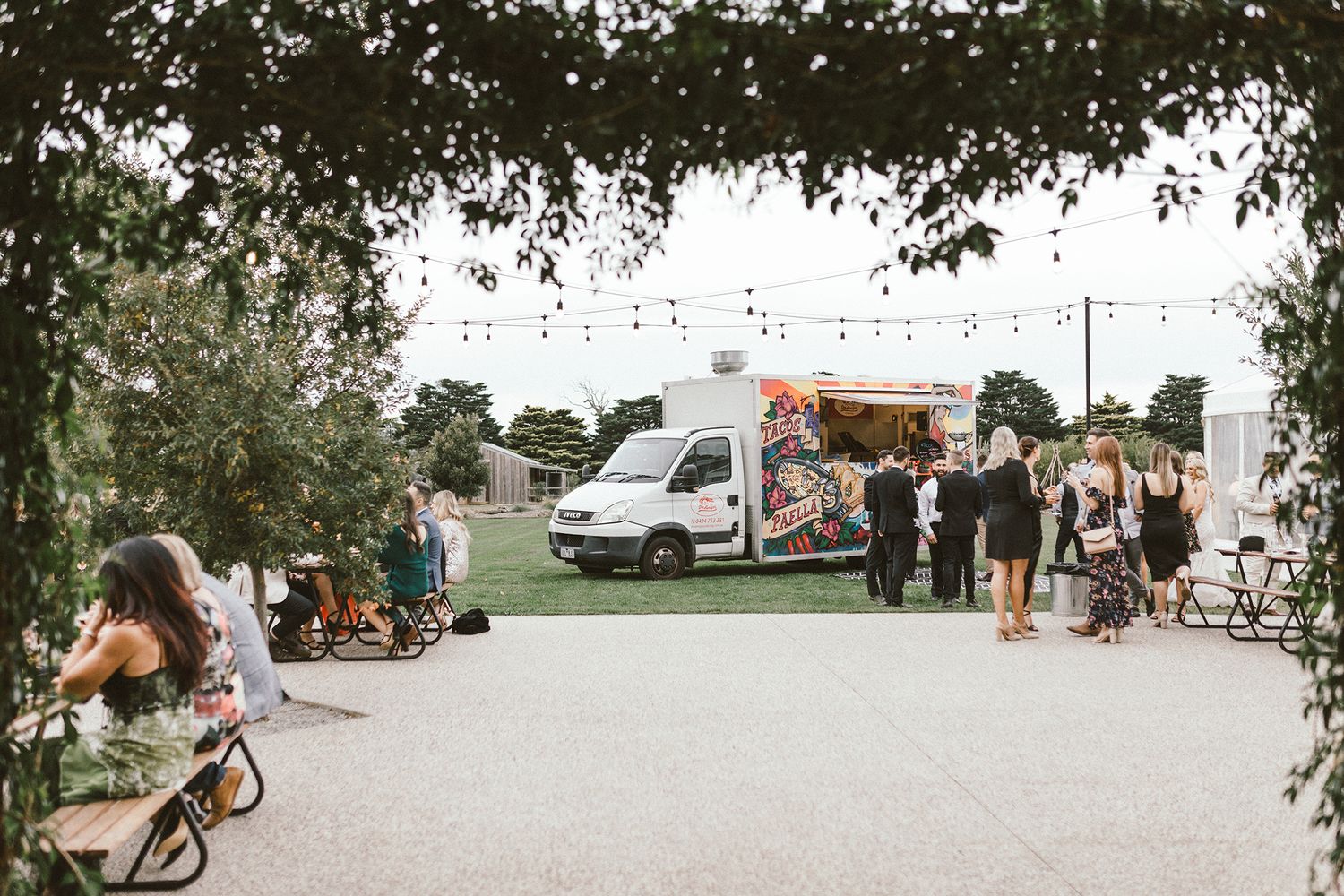 Food truck and guests at an outdoor wedding venue with string lights and trees.