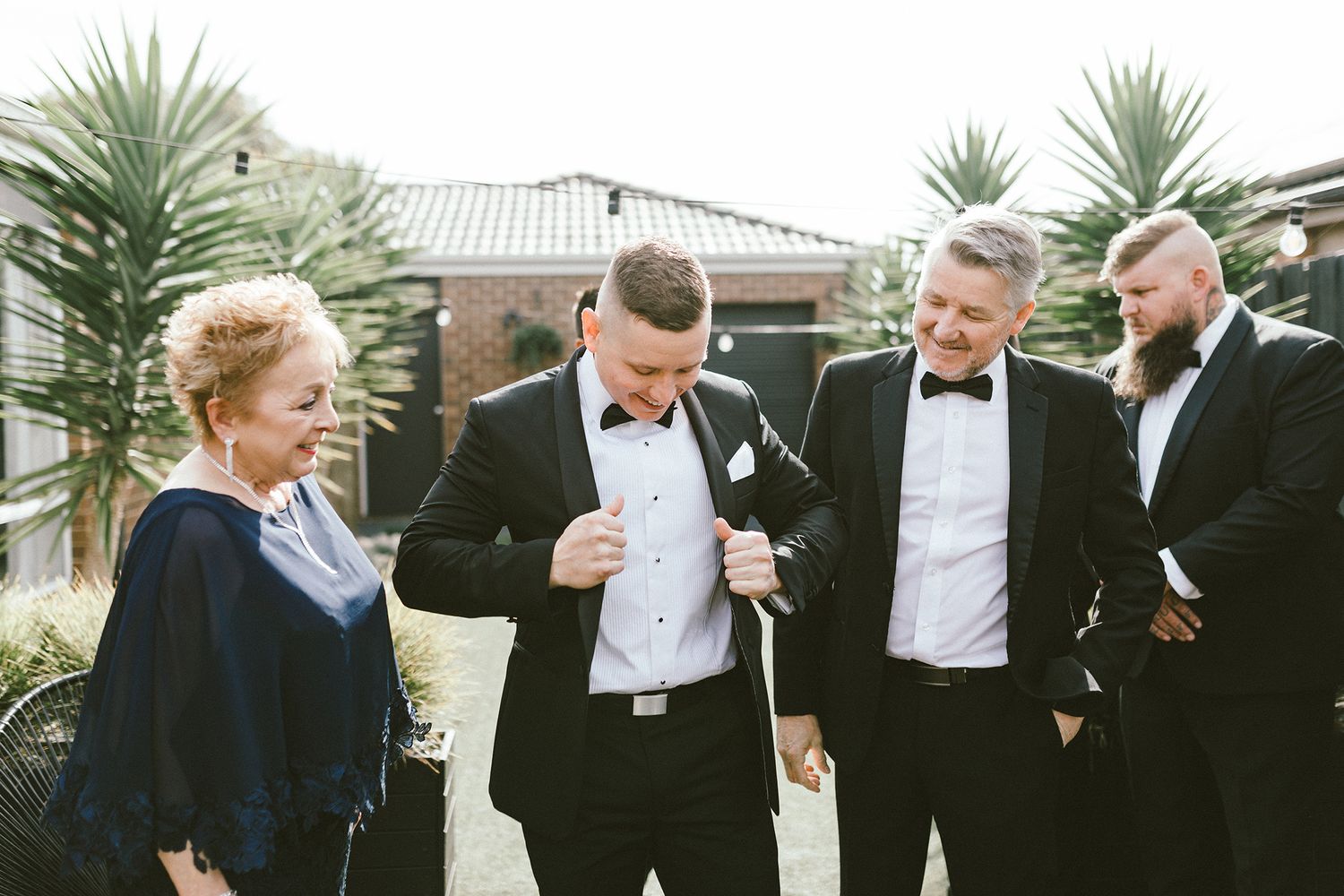 A group in formal attire share a lighthearted moment outdoors with palm trees in the background.