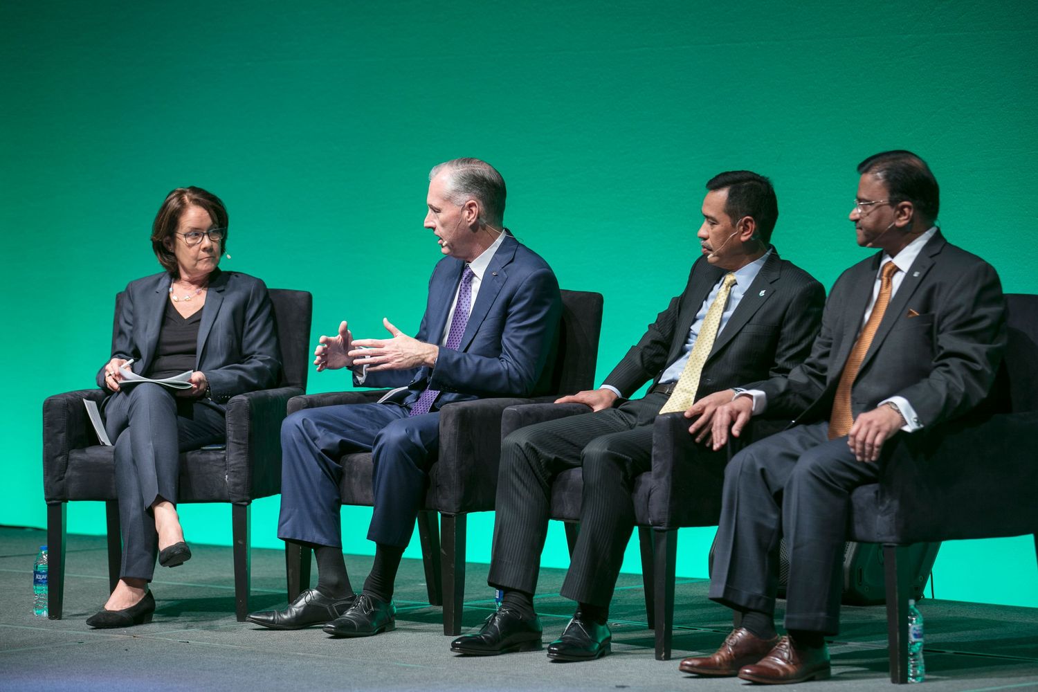Panel discussion taking place on stage with green backdrop at professional conference event.