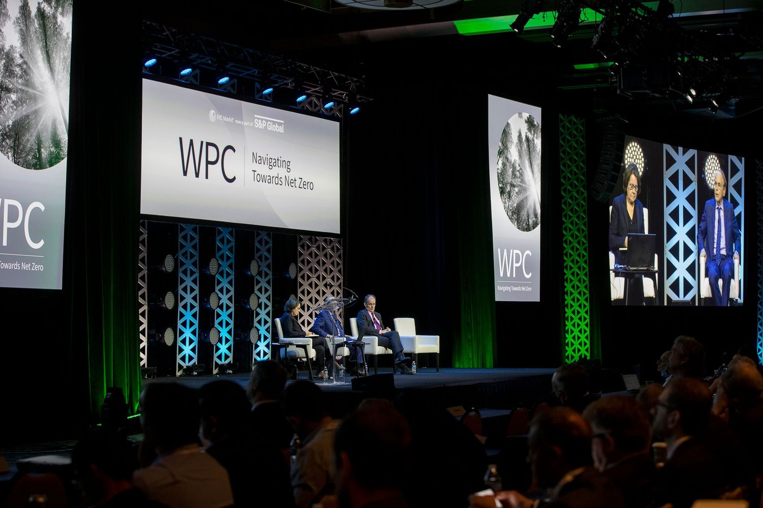 Professional conference stage setup with green lighting and multiple display screens showing presentations.