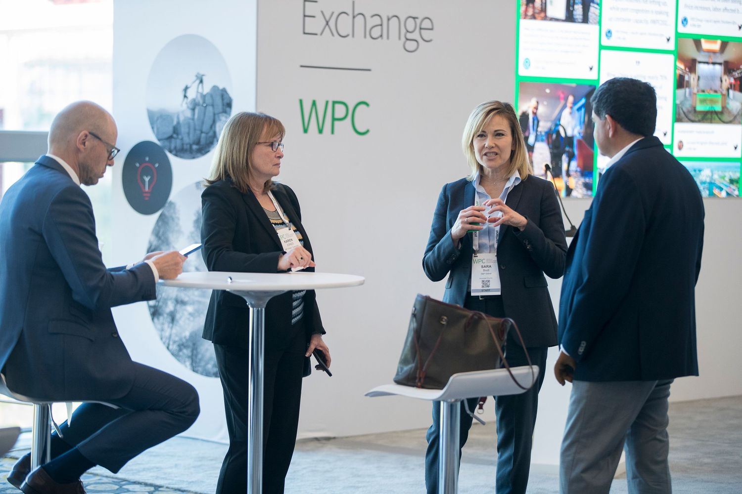 Corporate networking event with digital displays and attendees engaged in conversation.