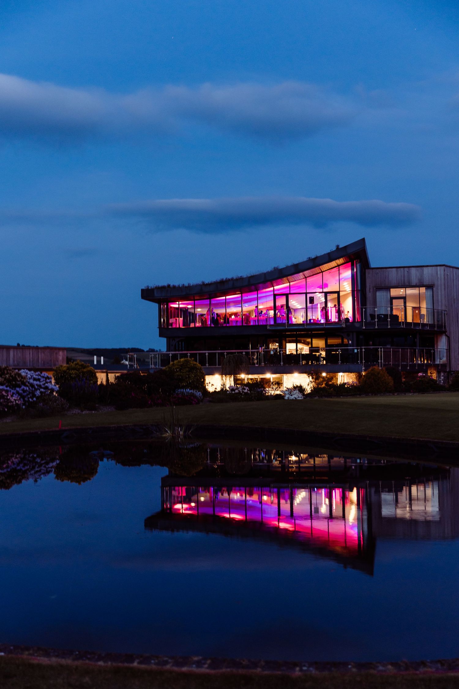 Modern venue building lit in purple at night with perfect reflection in pond.