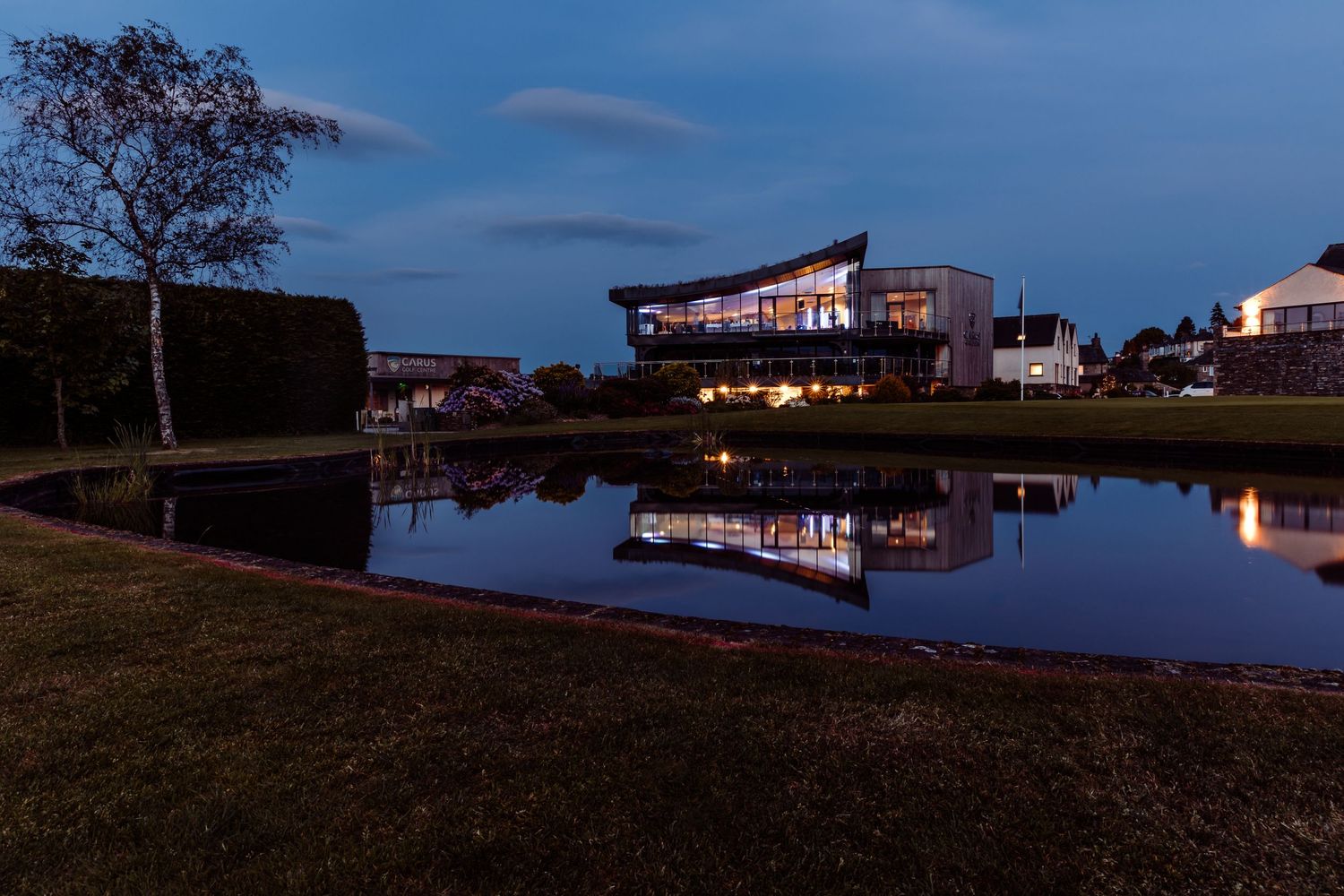 Event venue illuminated at dusk with reflection in still water.