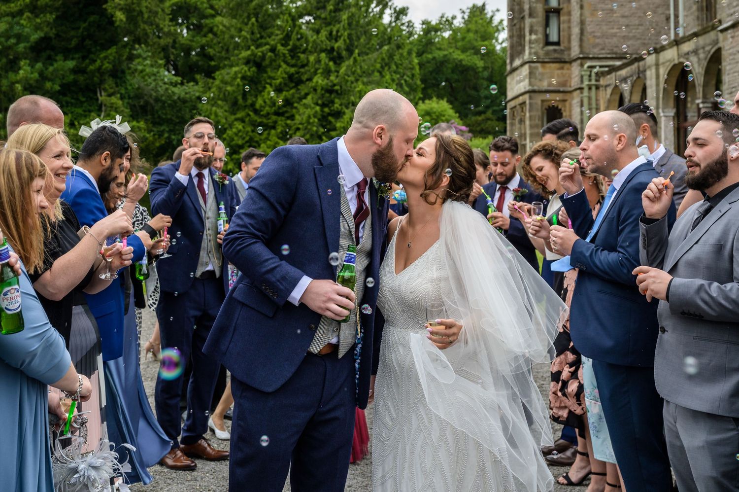Bride and groom kiss as guests blow bubbles at them at Armathwaite ~Hall wedding