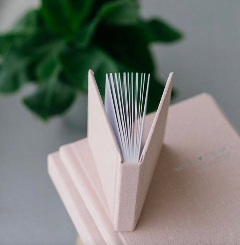Blush pink photo album with white pages fanned open against a gray background.