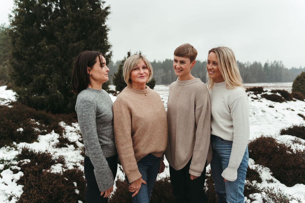 Four individuals in warm sweaters stand together on snowy ground outdoors.