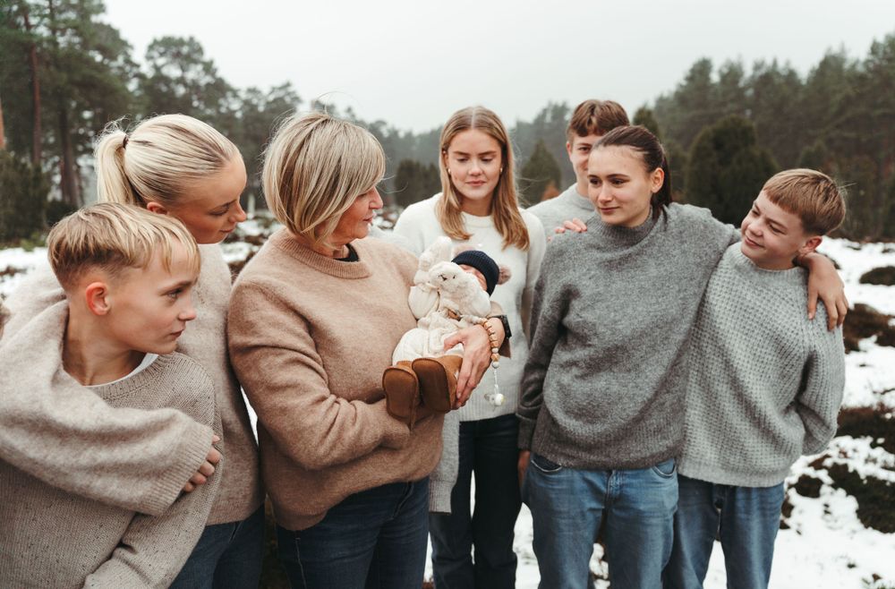 People in neutral sweaters share a laugh while gathered outdoors in the snow.