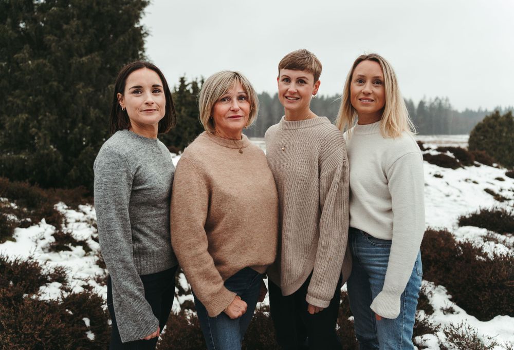 Group portrait of four people wearing coordinated neutral-colored sweaters in a winter setting.