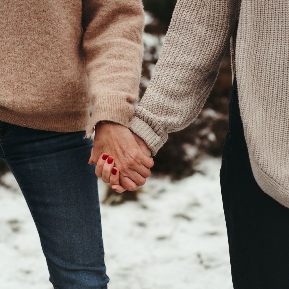 Close-up of two people holding hands while wearing cozy knit sweaters.