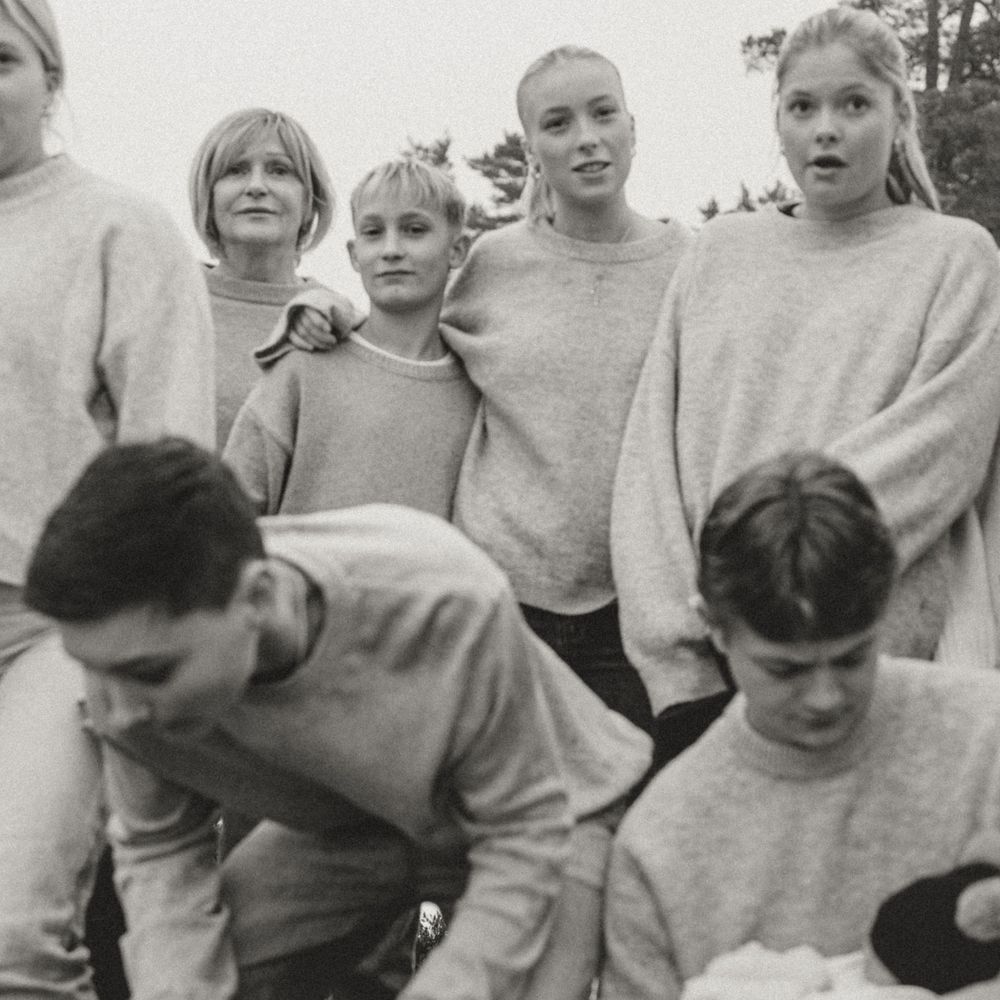 A black and white candid shot of people in light-colored sweaters gathering outdoors.