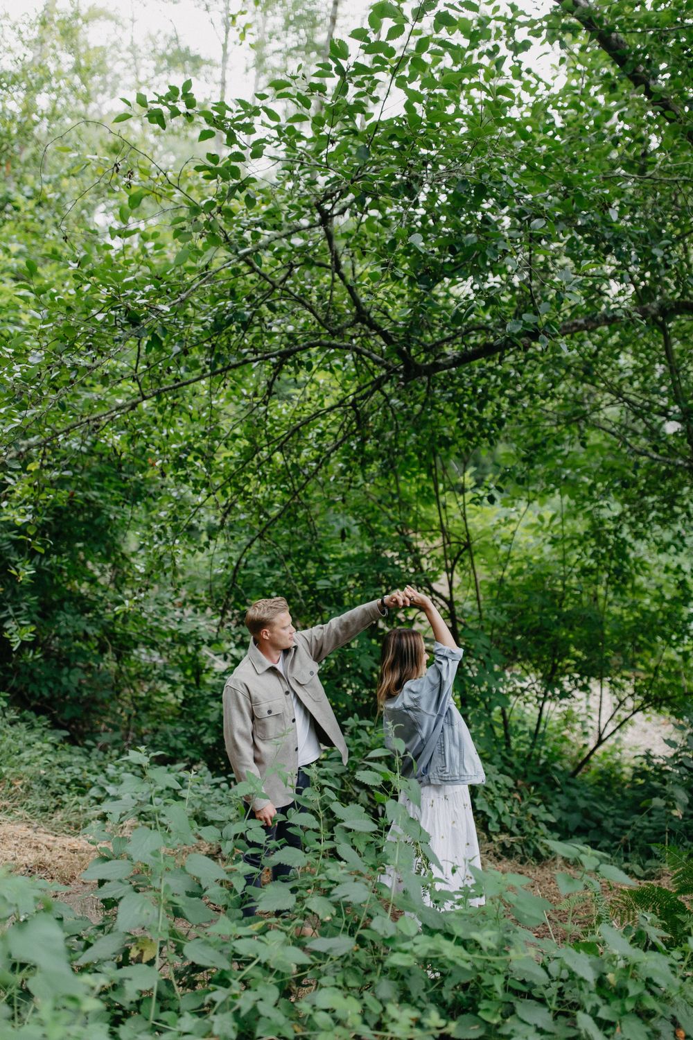 A couple dances playfully together on a wooded trail surrounded by green foliage.