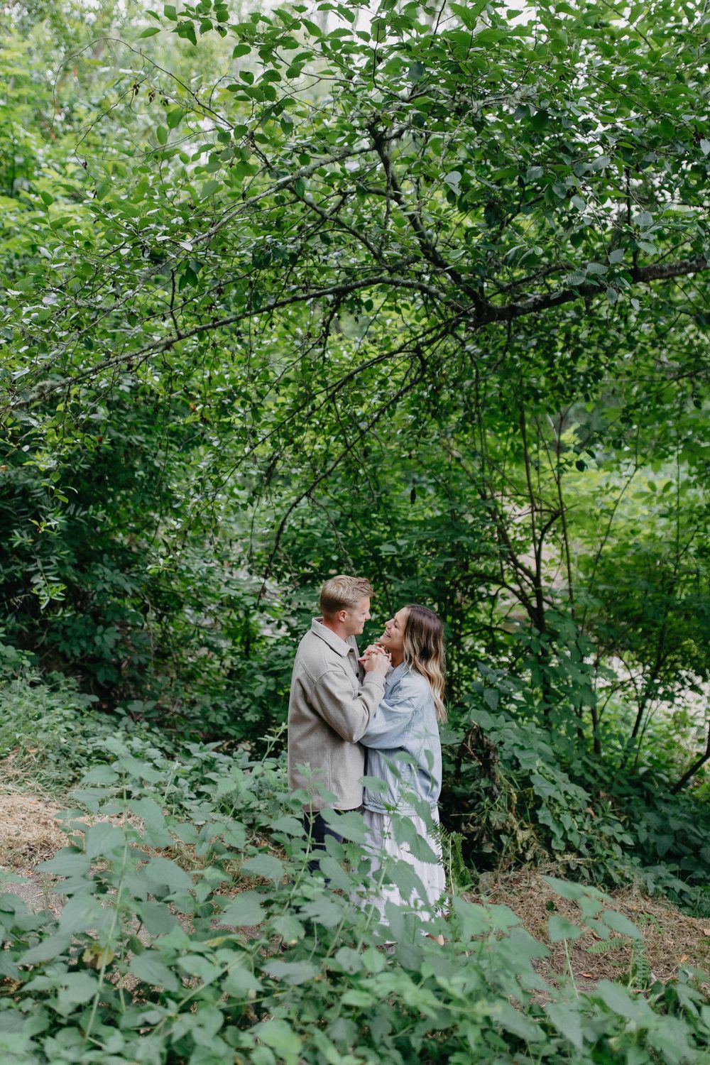 A tender embrace between a couple on a nature path surrounded by green leaves.