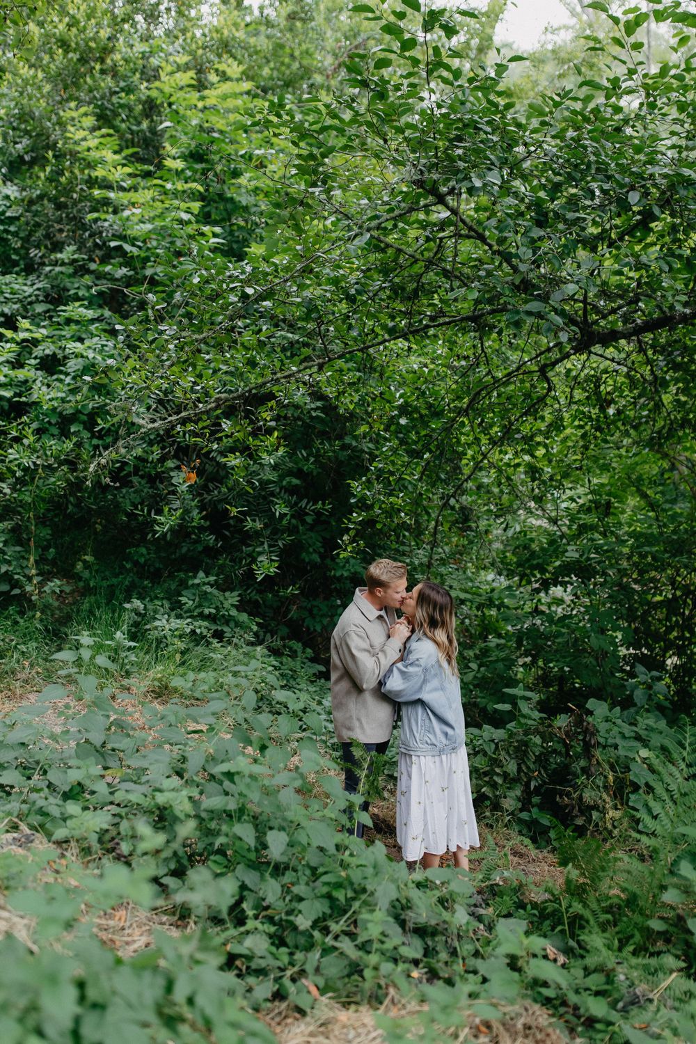 A loving couple shares a romantic moment on a forest trail surrounded by greenery.