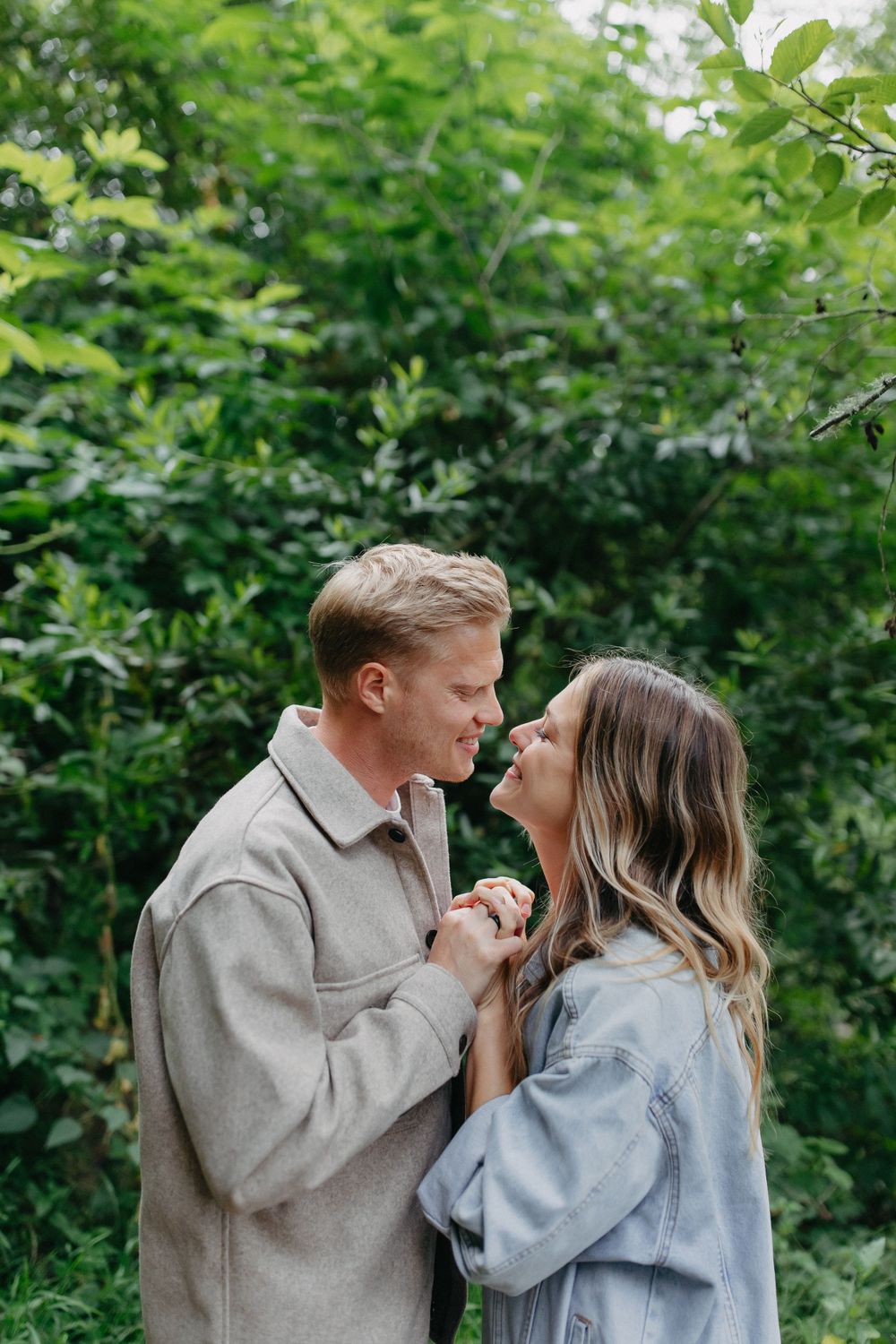 A couple in matching light-colored jackets shares an intimate moment in a green garden setting.
