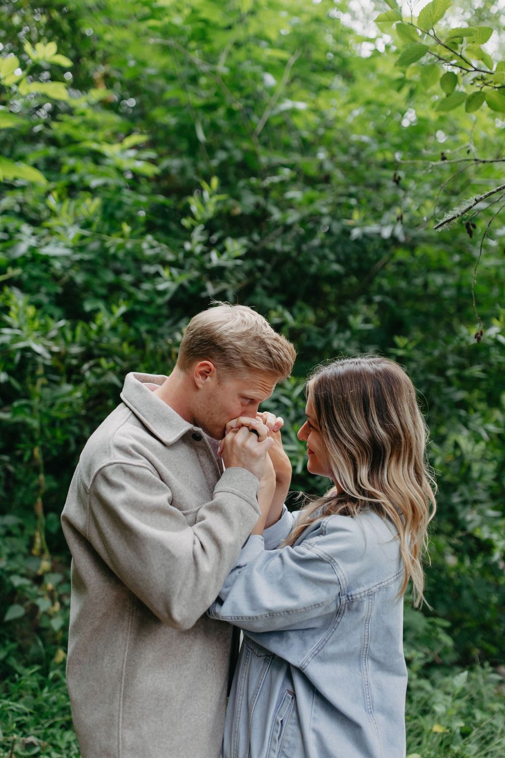 A couple holds hands tenderly against a backdrop of lush green foliage.