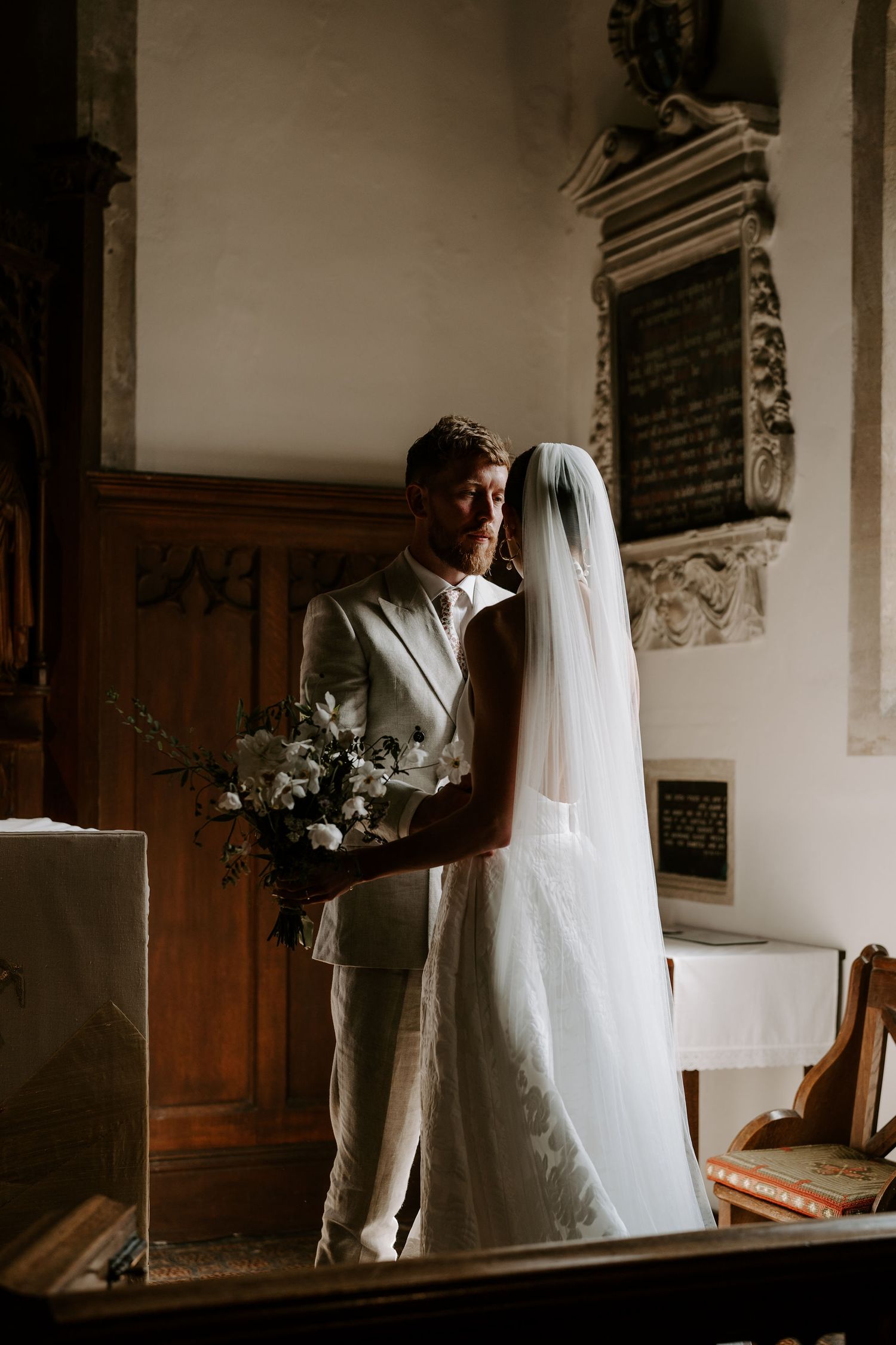 groom staring at bride in atmospheric lighting at st Nicholas church in Oxfordshire