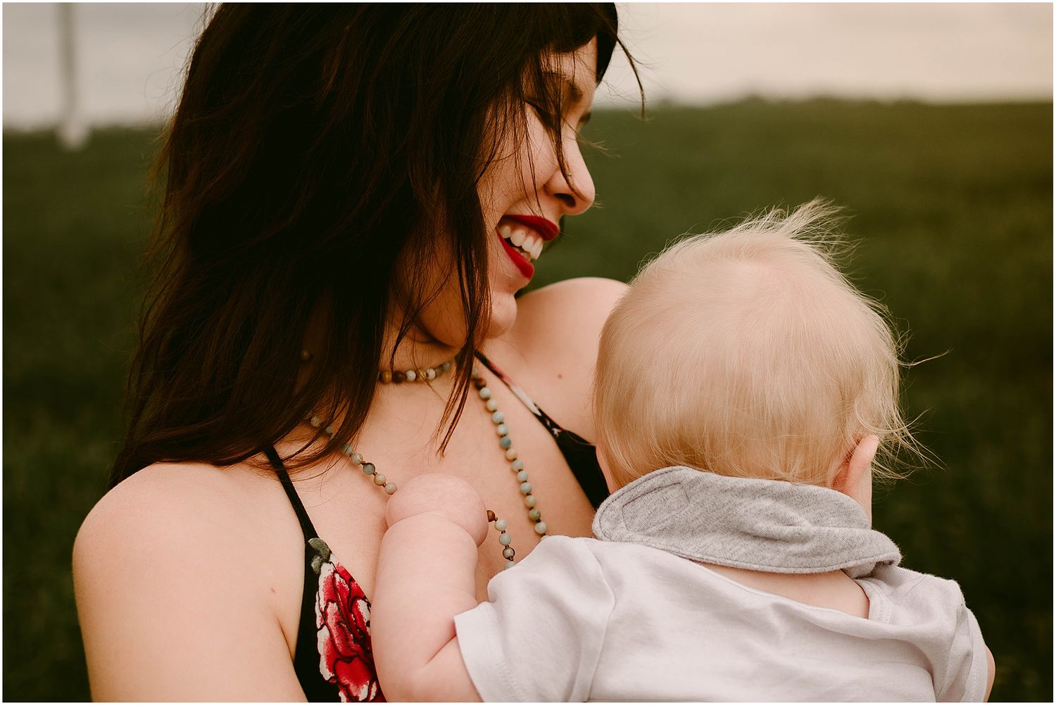 Close-up of a baby resting against a woman wearing a necklace and floral top.