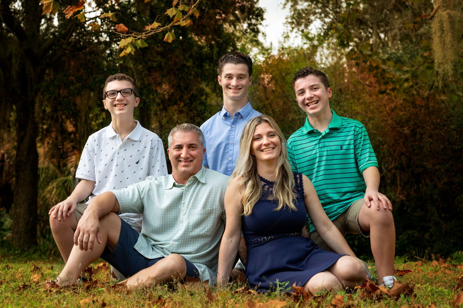 Family sitting together smiling in the grass at the park.