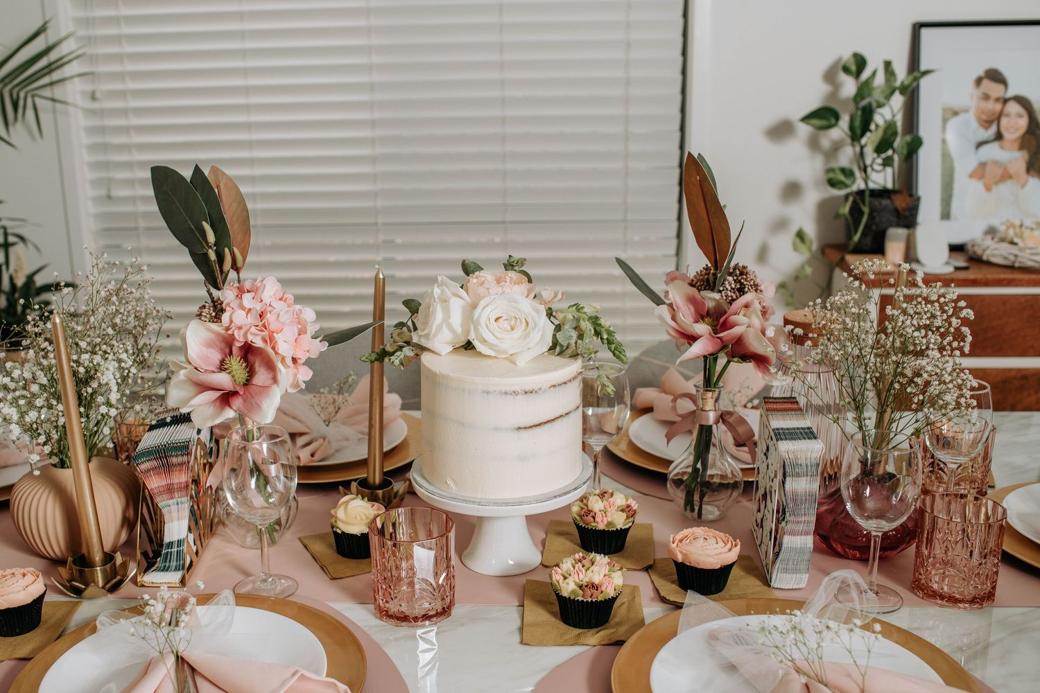 Elegant wedding reception table with white cake, pink flowers, and rose gold accents.