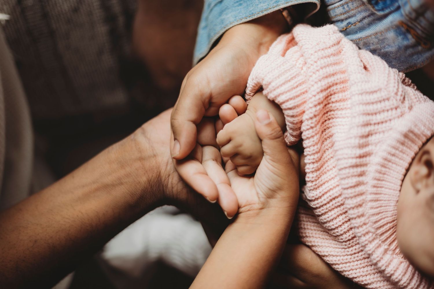Close up of hands holding a newborn baby wrapped in pink.