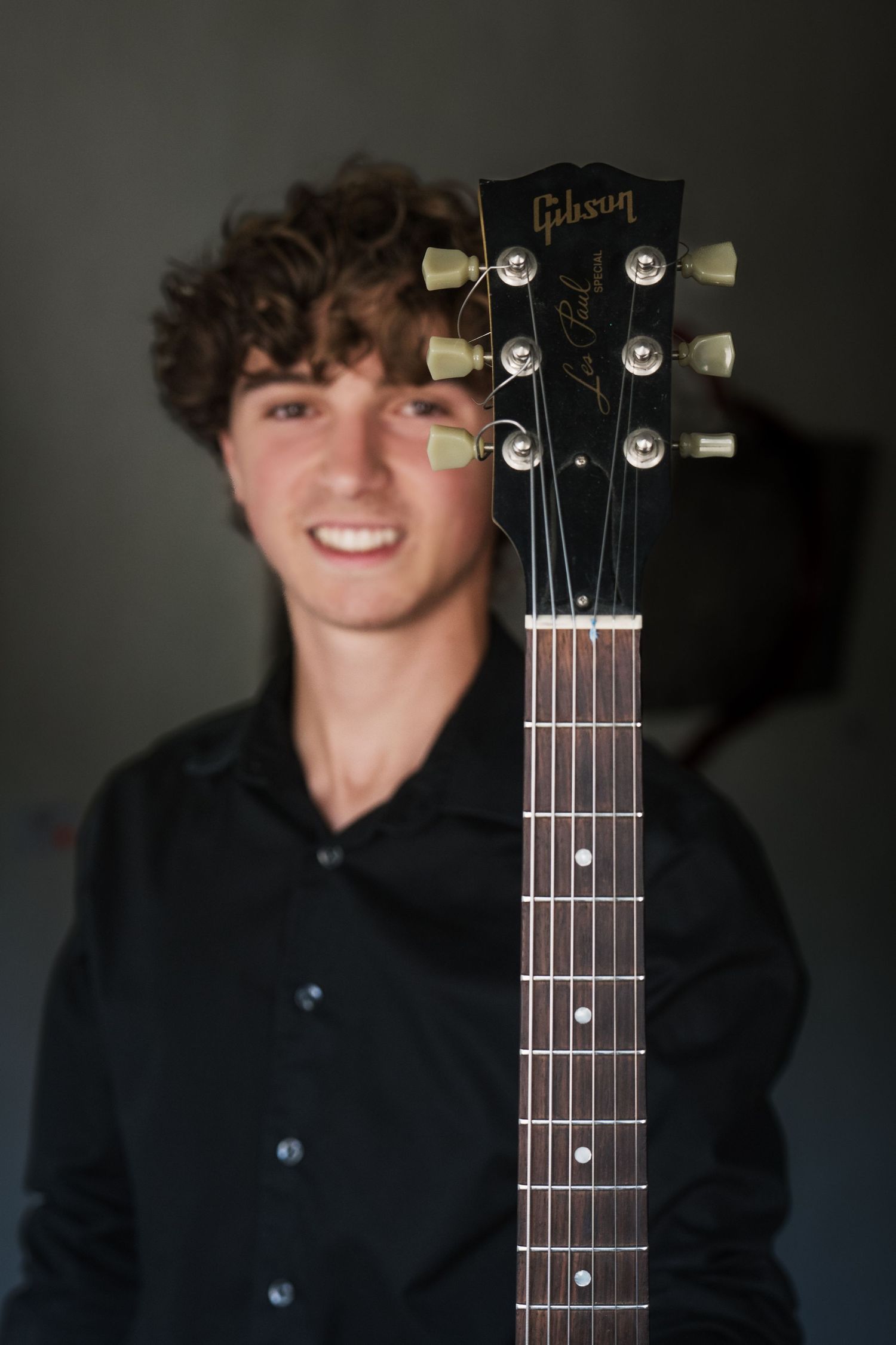 Senior portrait of boy smiling, holding his guitar, the head of guitar is in focus, shot by Milwaukee senior photographer Rachel Dickman.