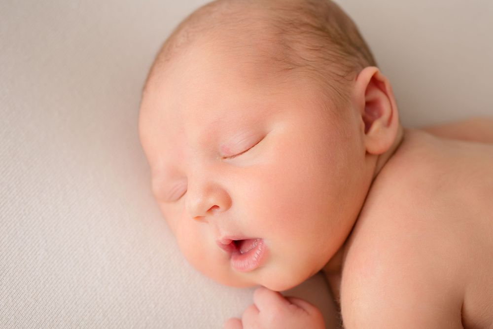 Sleeping newborn baby with parted lips captured in soft natural light.