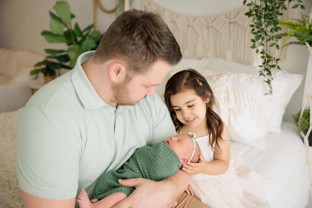 Tender family moment shared on bed with macrame wall hanging and green plants in background.