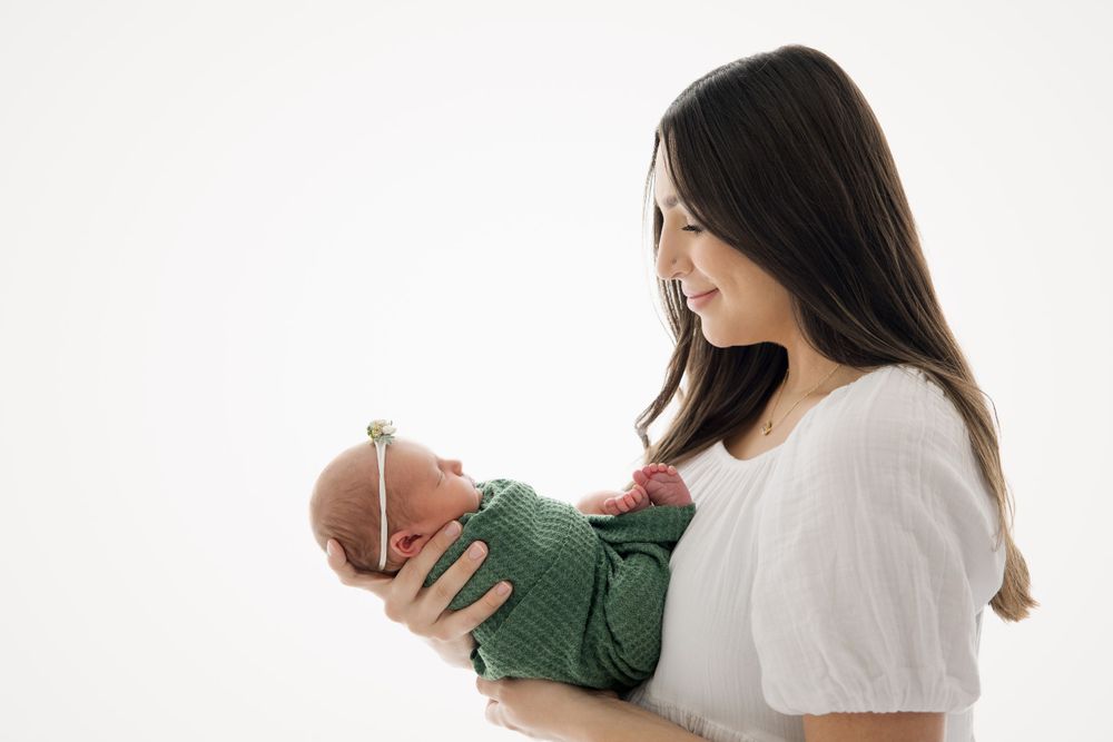 A tender moment as a parent cradles a newborn baby wrapped in a sage green outfit against a white backdrop.