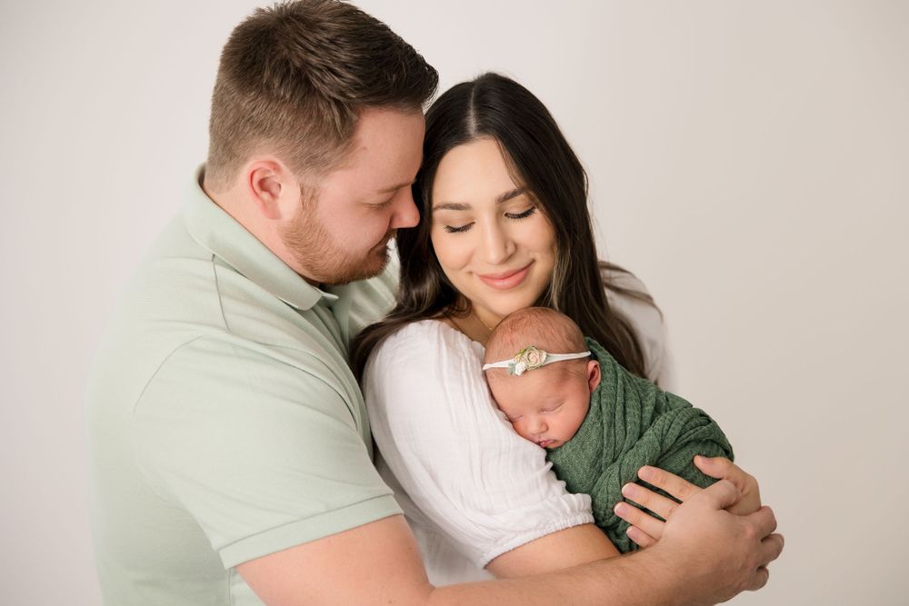 An intimate family moment with a swaddled newborn being held close by parents against a neutral backdrop.