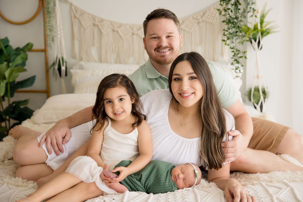Family portrait showing tender moment together on bed with bohemian-styled wall decor and plants.