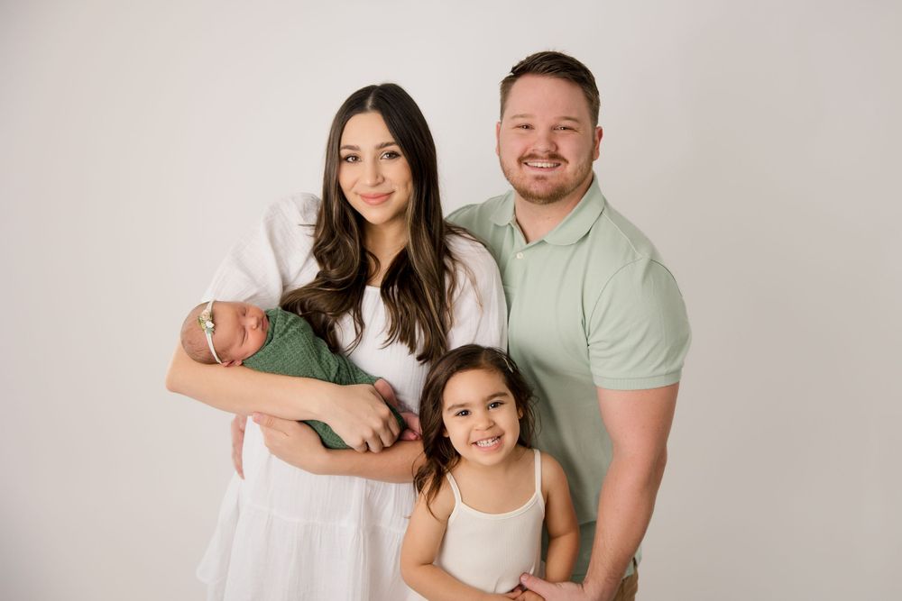 Family of four in casual white attire against neutral studio backdrop.